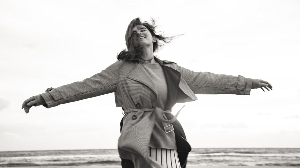 Woman in a coat feeling free on a windy beach day in black and white photography.
